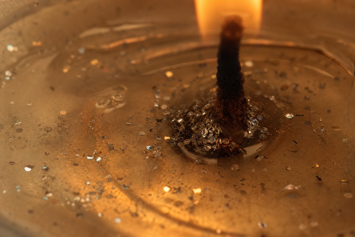 Macro-opname van gesmolten doorzichtige was bij de lont van een brandende kaars, waarin kleine zilveren glittertjes naar beneden zakken.