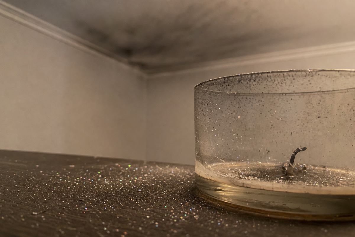 Kleine glittertjes verspreid over de tafel rond een opgebrande kaars, op de achtergrond een dunne grijze roetfilm op het plafond.
