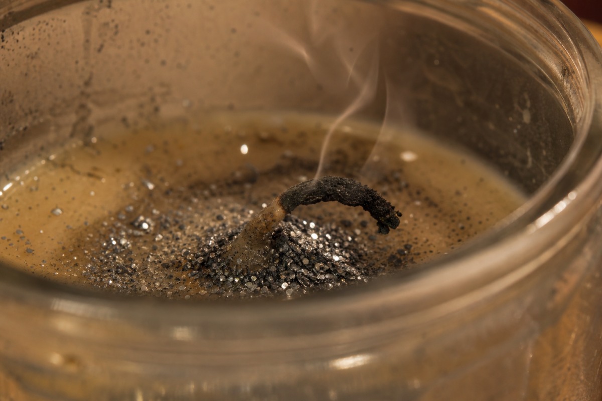 Een geknikte, verkoolde lont omhuld met opgehoopte zilveren glitter in gestolde was, de kaars is gedoofd.