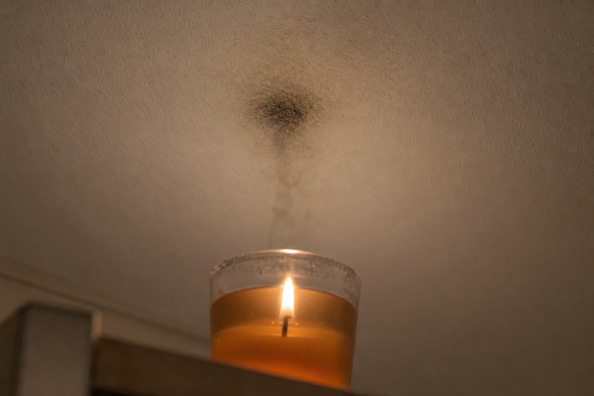 Donkere roetvlek op een wit plafond, recht boven een brandende gelkaars in een glazen potje